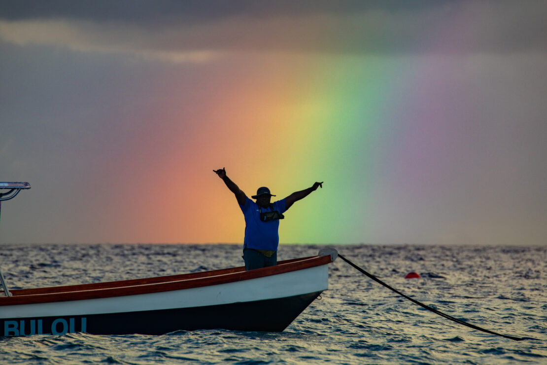 man on boat with rainbow in background over water